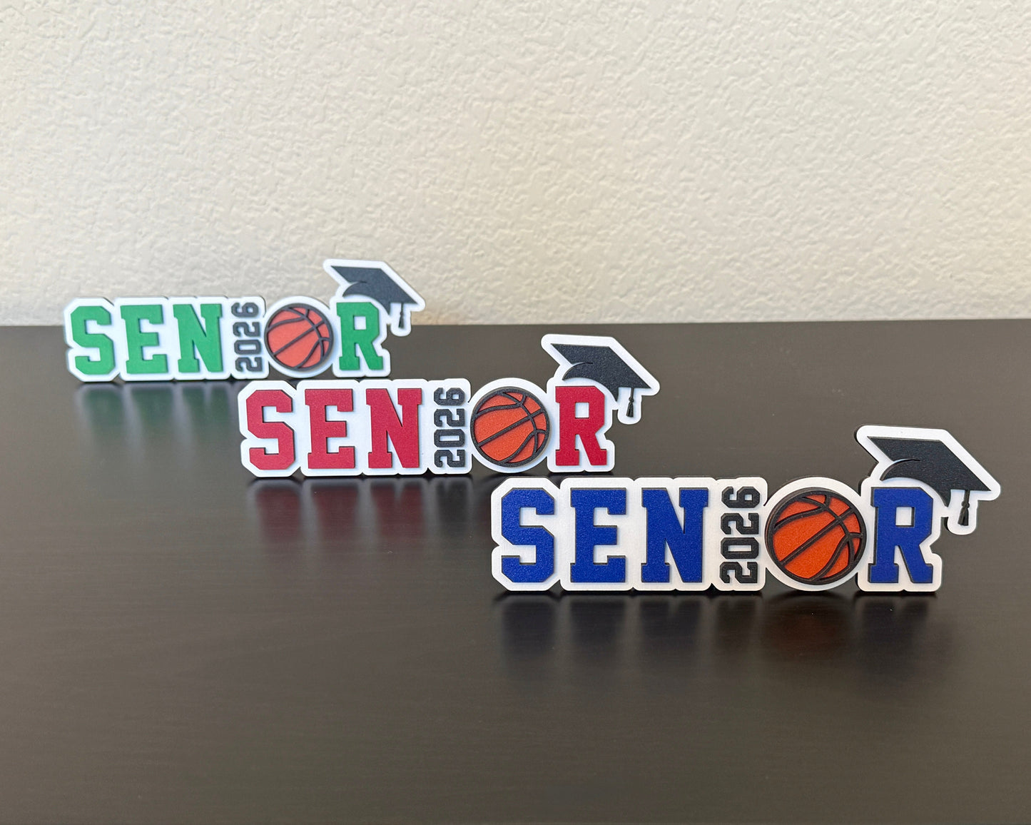 High School Senior Class of 2026 basketball signs for graduation by Half Turn Designs. Shown here in white wood with green, red and blue accents.