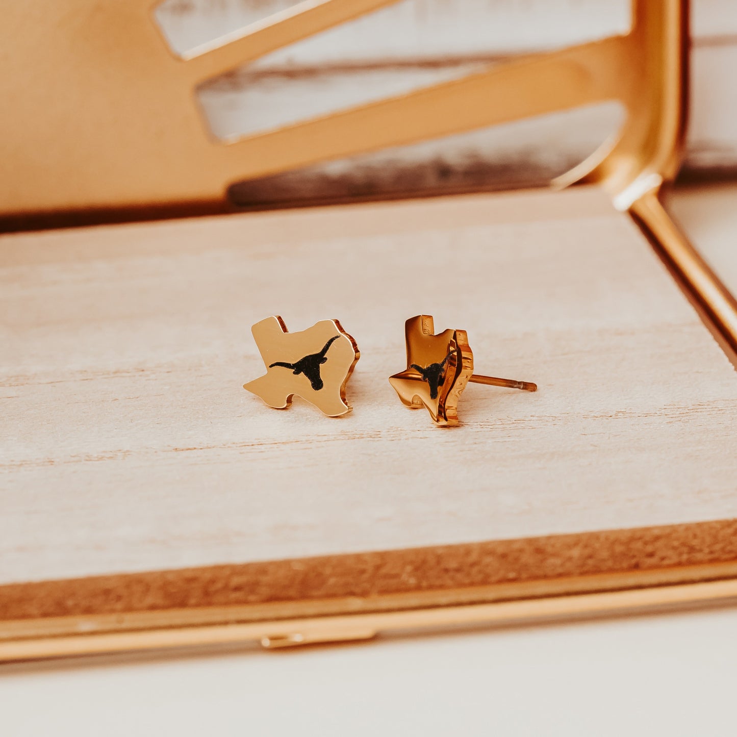 University of Texas Longhorns stainless steel stud earrings shaped like the state of Texas, engraved with the UT Longhorn logo. Shown in 12mm size on Half Turn Designs branded earring cards, available in gold and silver finishes. Shown here in gold finish.