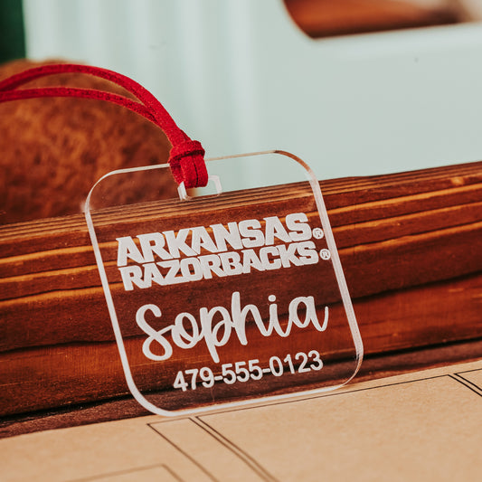 Officially licensed Arkansas Razorbacks acrylic luggage tags in frosted, clear, red, and black, personalized with names and phone numbers. Shown here in clear acrylic