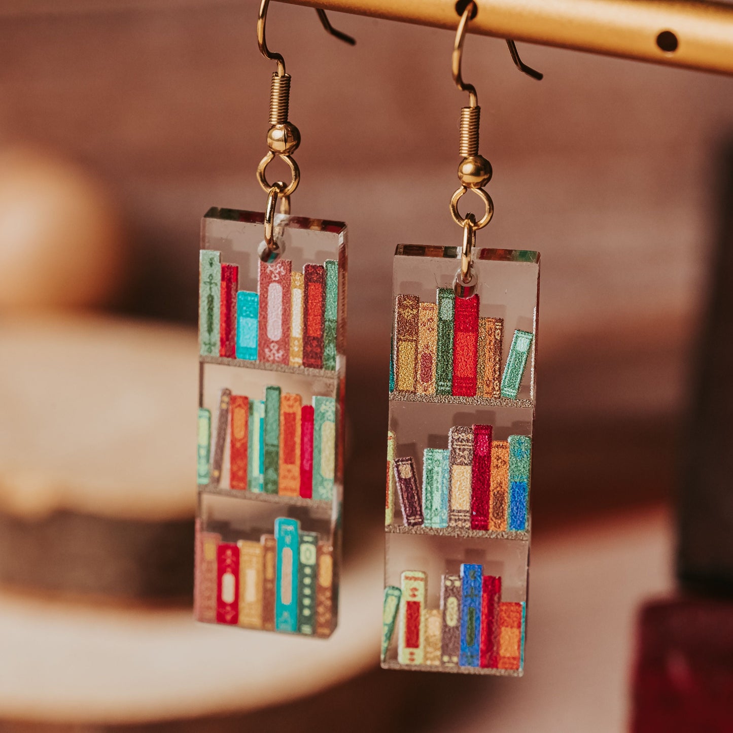 Book lover earrings with tiny bookshelf designs printed on clear acrylic, shown hanging on gold tone earring hooks