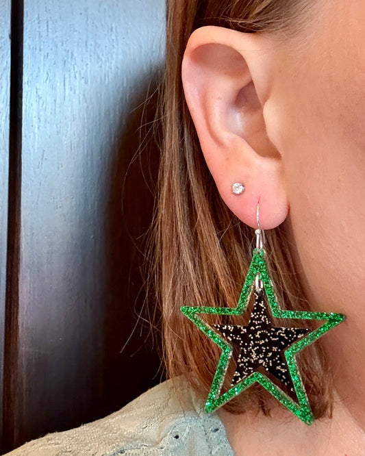 Model wearing Green and black glitter stars earrings on silver hooks, lightweight acrylic dangles for game day, handmade in Texas by half turn designs