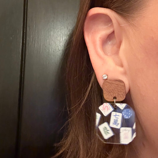 Model wearing Mahjong dangle earrings with blue Chinoiserie mahjong tile and dice pattern acrylic, scalloped square shape, topped with walnut wood stud and stainless steel post, handmade mahjong jewelry for women by Half Turn Designs