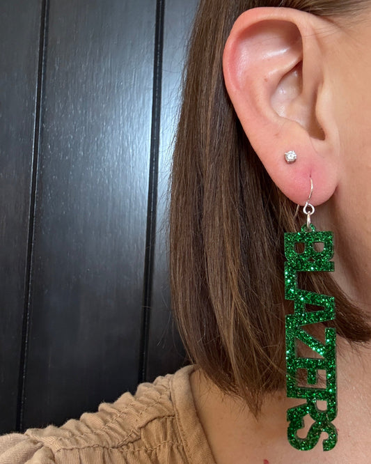 Model wearing UAB game day Blazers earring dangles in green glitter acrylic