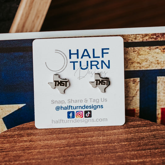 Silver stainless steel Texas-shaped TXST stud earrings on a wooden surface