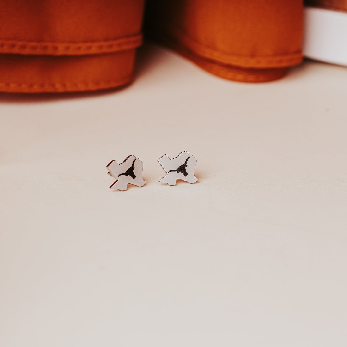 University of Texas stainless steel stud earrings shaped like the state of Texas, engraved with the Longhorn logo. Shown in 12mm size on Half Turn Designs branded earring cards, available in gold and silver finishes. Shown here in silver finish.
