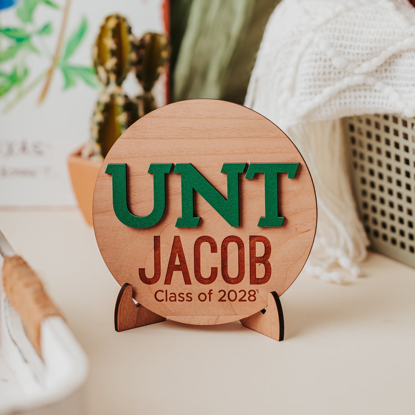 Officially licensed University of North Texas 5 inch round wooden dorm decor, shelf sitter and desk sign in cherry wood with the UNT letters in Mean Green, personalized with your choice of 1-2 lines of engraved text in four wood finishes. Comes with a matching stand.