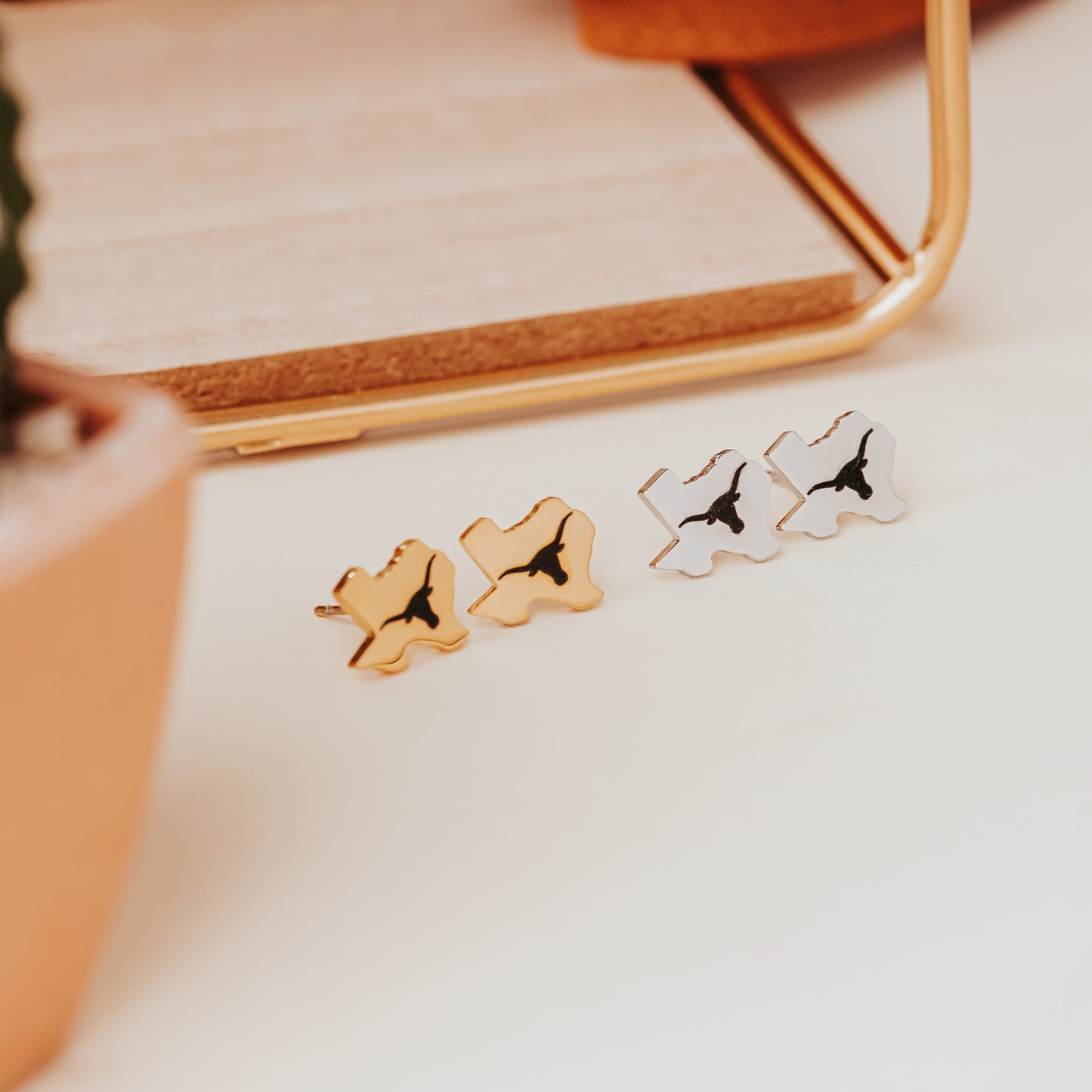University of Texas stainless steel stud earrings shaped like the state of Texas, engraved with the Longhorn logo. Shown in 12mm size on Half Turn Designs branded earring cards, available in gold and silver finishes.