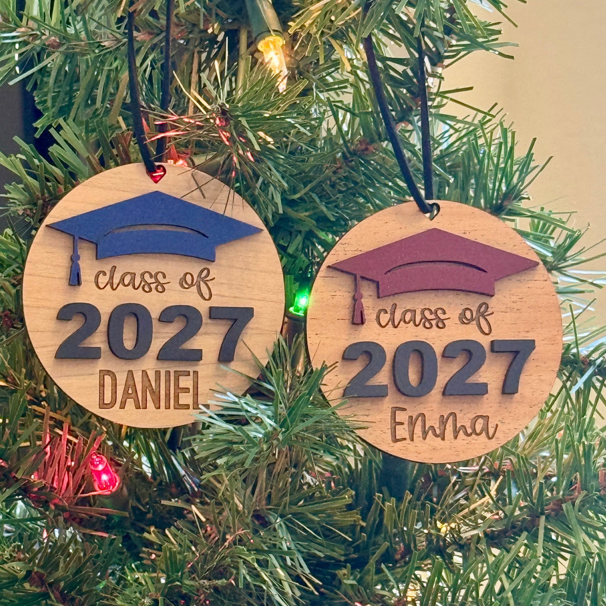 Personalized Class of 2027 wooden ornaments in cherry and mahogany finish with blue and maroon graduation caps, raised black 2027 numbers and graduate's engraved names