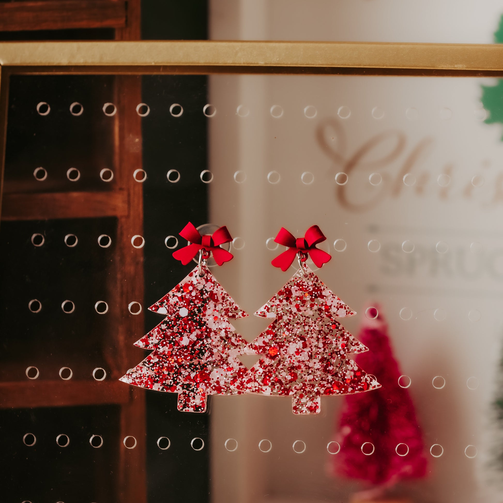 Red and white glitter acrylic Christmas tree earrings with red bow studs, lightweight with 2 inch drop length, holiday dangles styled on a neutral background.