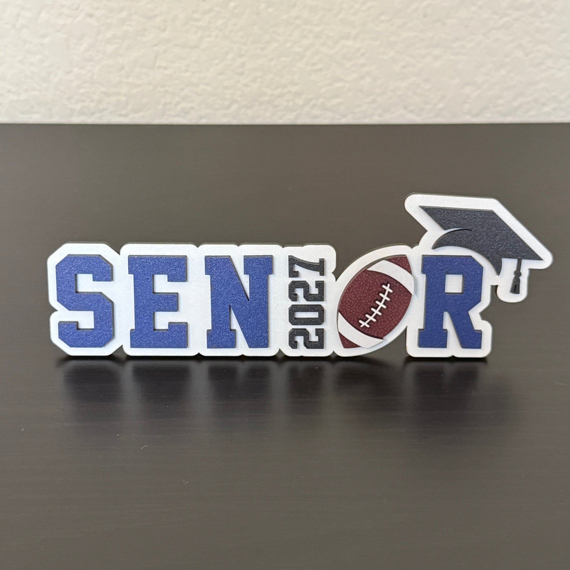 Class of 2027 football senior sign with white wood base, green letters, 2027 as the I, football as the O, and black cap.