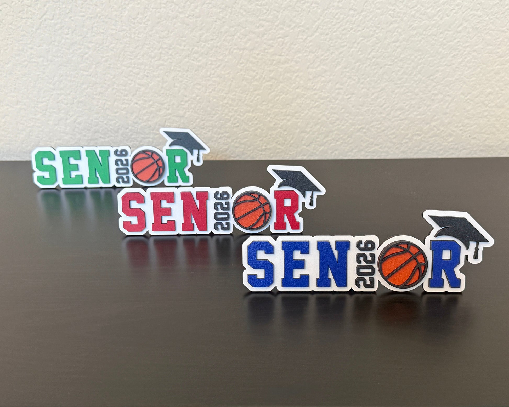 High School Senior Class of 2026 basketball signs for graduation by Half Turn Designs. Shown here in white wood with green, red and blue accents.
