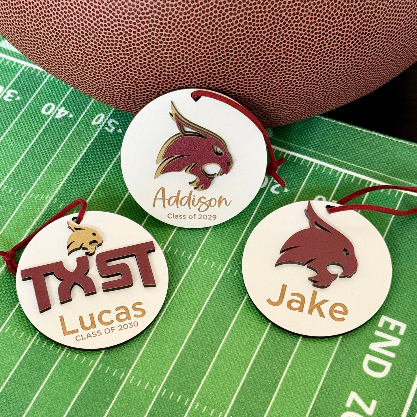 Texas State University ornament collection by Half Turn Designs. Three wooden 3" round ornaments. From left to right - Maroon TXST with Gold bobcat design, Two layer gold and maroon bobcat and maroon bobcat. Each Ornament personalized with 1-2 lines of text such as name and year of graduation.