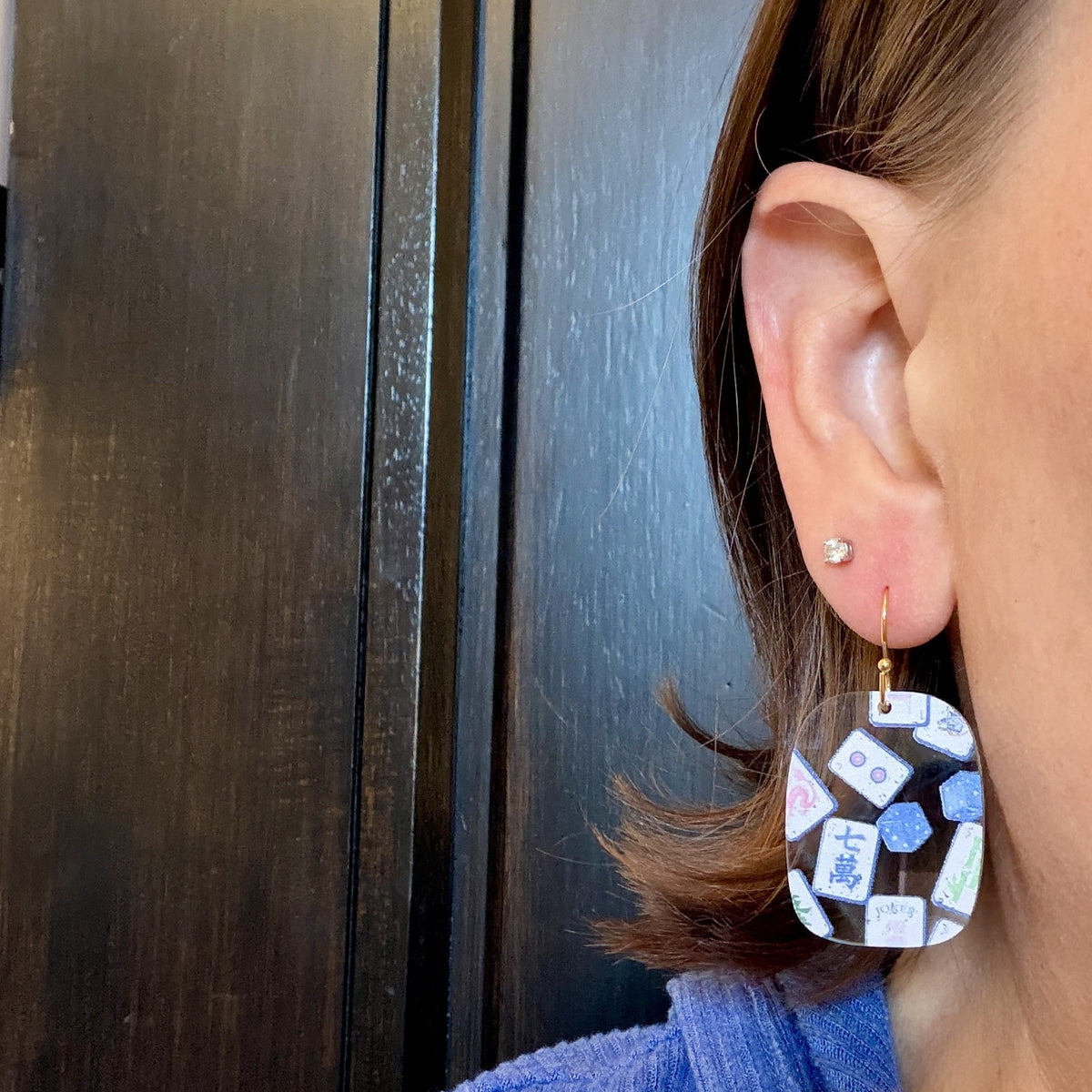 Model wearing Blue chinoiserie mahjong tile earrings in clear acrylic with mahjong tile and dice print on gold-tone hooks