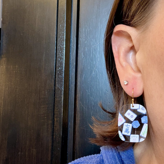 Model wearing Blue chinoiserie mahjong tile earrings in clear acrylic with mahjong tile and dice print on gold-tone hooks