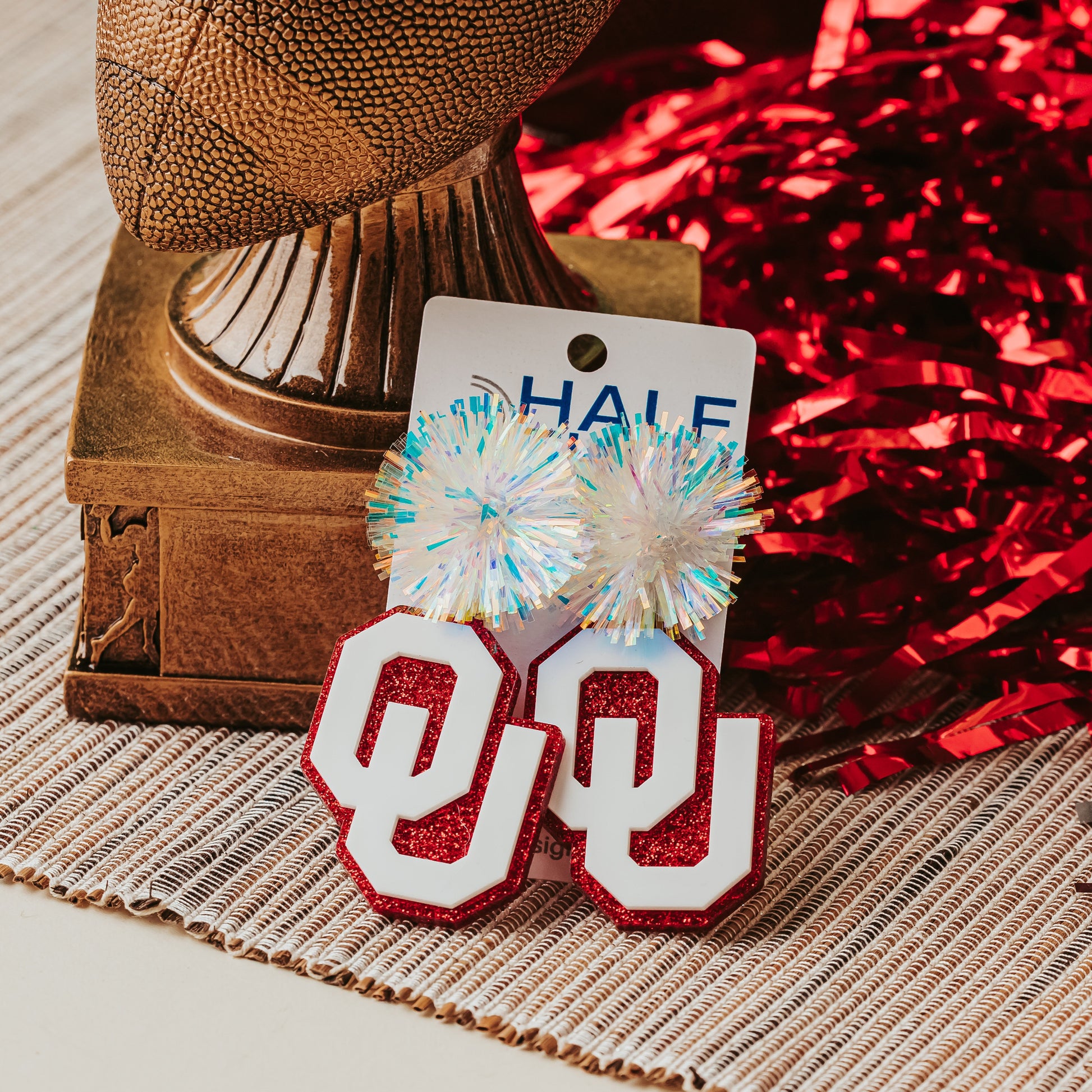 Officially licensed University of Oklahoma game day earring collection by Half Turn Designs. These earrings are available in combinations of crimson and white acrylic, including glitter. Available in a eight different fun toppers for OU game days and as a gift for your favorite Oklahoma Sooner.  White on Crimson Glitter with Iridescent Tinsel Toppers shown here.