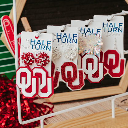 Officially licensed University of Oklahoma game day earring collection by Half Turn Designs. These earrings are available in combinations of crimson and white acrylic, including glitter. Available in a eight different fun toppers for OU game days and as a gift for your favorite Oklahoma Sooner.