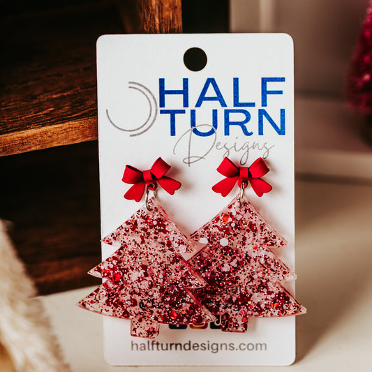 Red and white glitter acrylic Christmas tree earrings with red bow studs, lightweight with 2 inch drop length, holiday dangles styled on a neutral background.