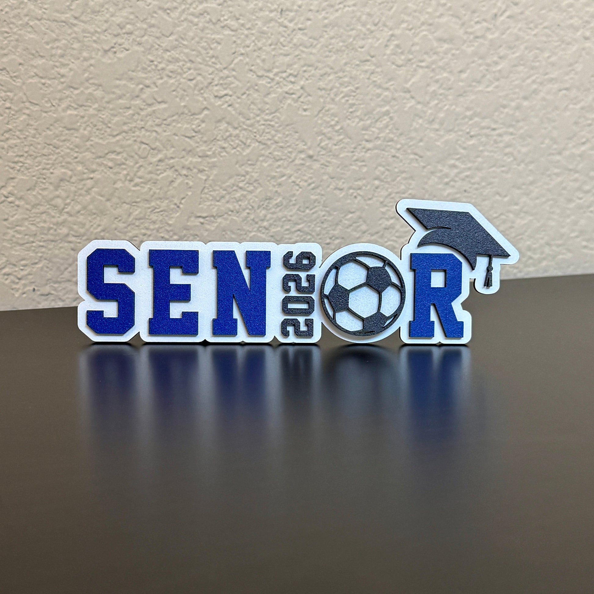 Class of 2026 senior soccer sign with blue and white lettering, soccer ball design and graduation cap accent, tabletop decor for high school soccer graduation party or senior sports banquet