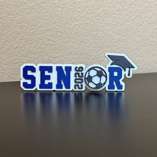 Class of 2026 senior soccer sign with blue and white lettering, soccer ball design and graduation cap accent, tabletop decor for high school soccer graduation party or senior sports banquet
