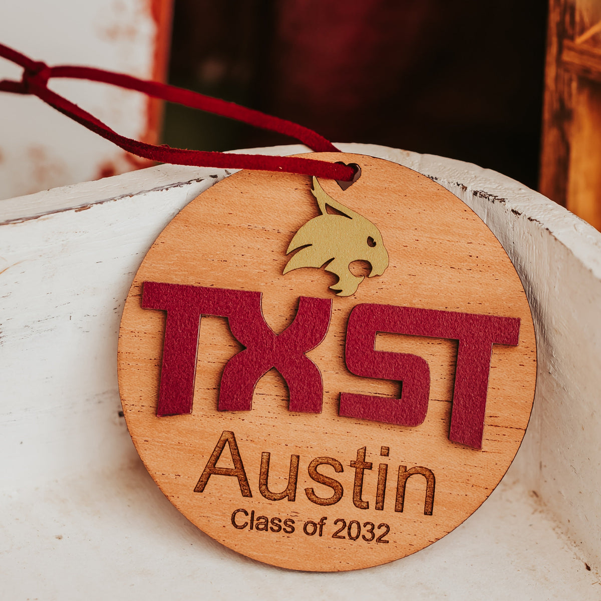 Mahogany Texas State ornament with gold Bobcat, maroon TXST letters and an engraved name and class year on a maroon cord