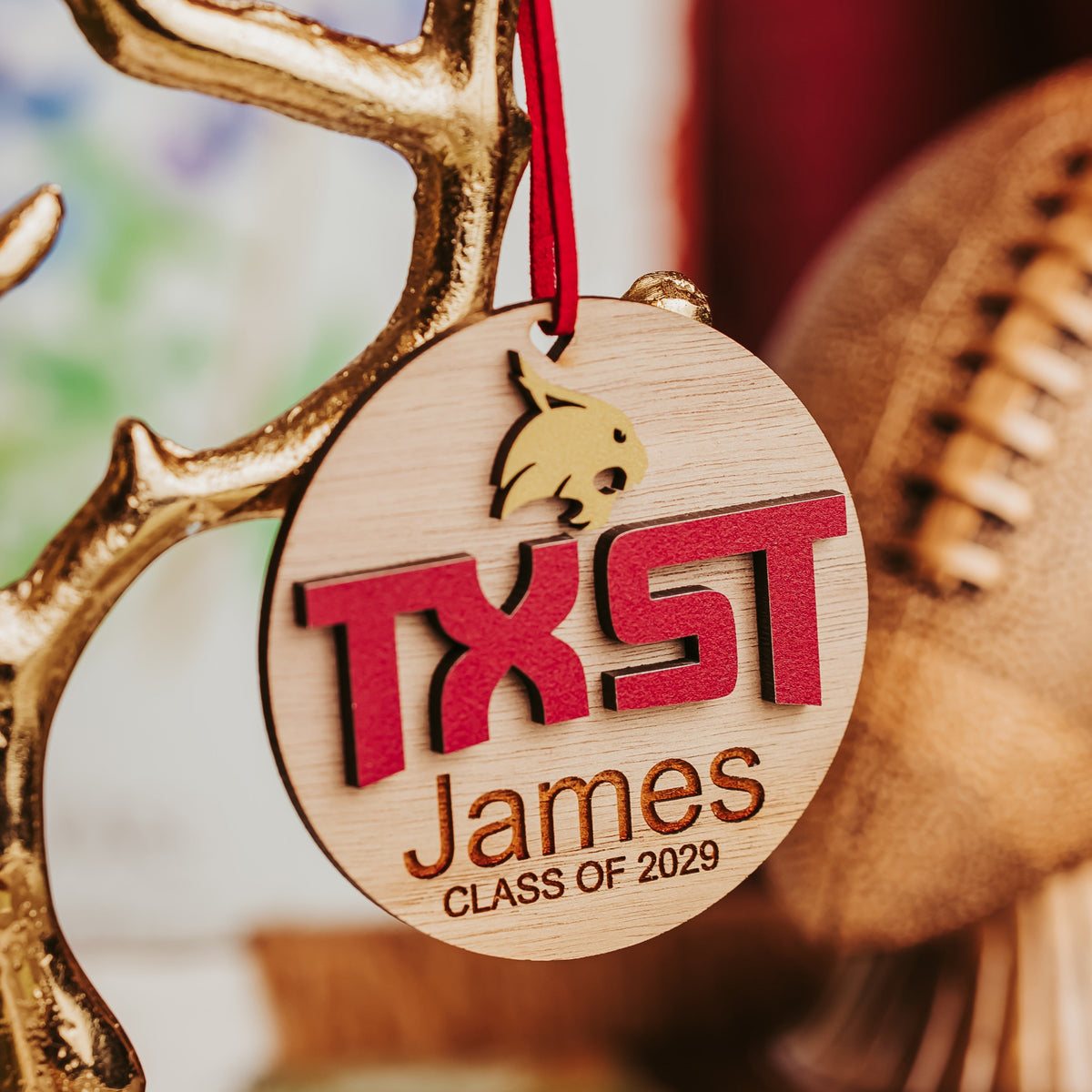 Walnut Texas State ornament in dark wood grain with gold Bobcat, maroon TXST letters and engraved name on a maroon cord