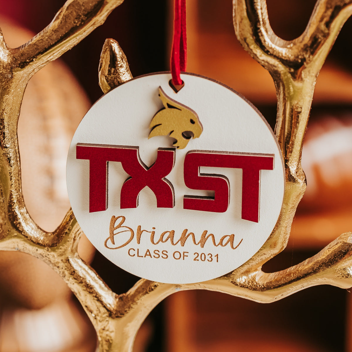 White personalized Texas State University ornament with gold Bobcat, maroon TXST letters and engraved name on a maroon cord