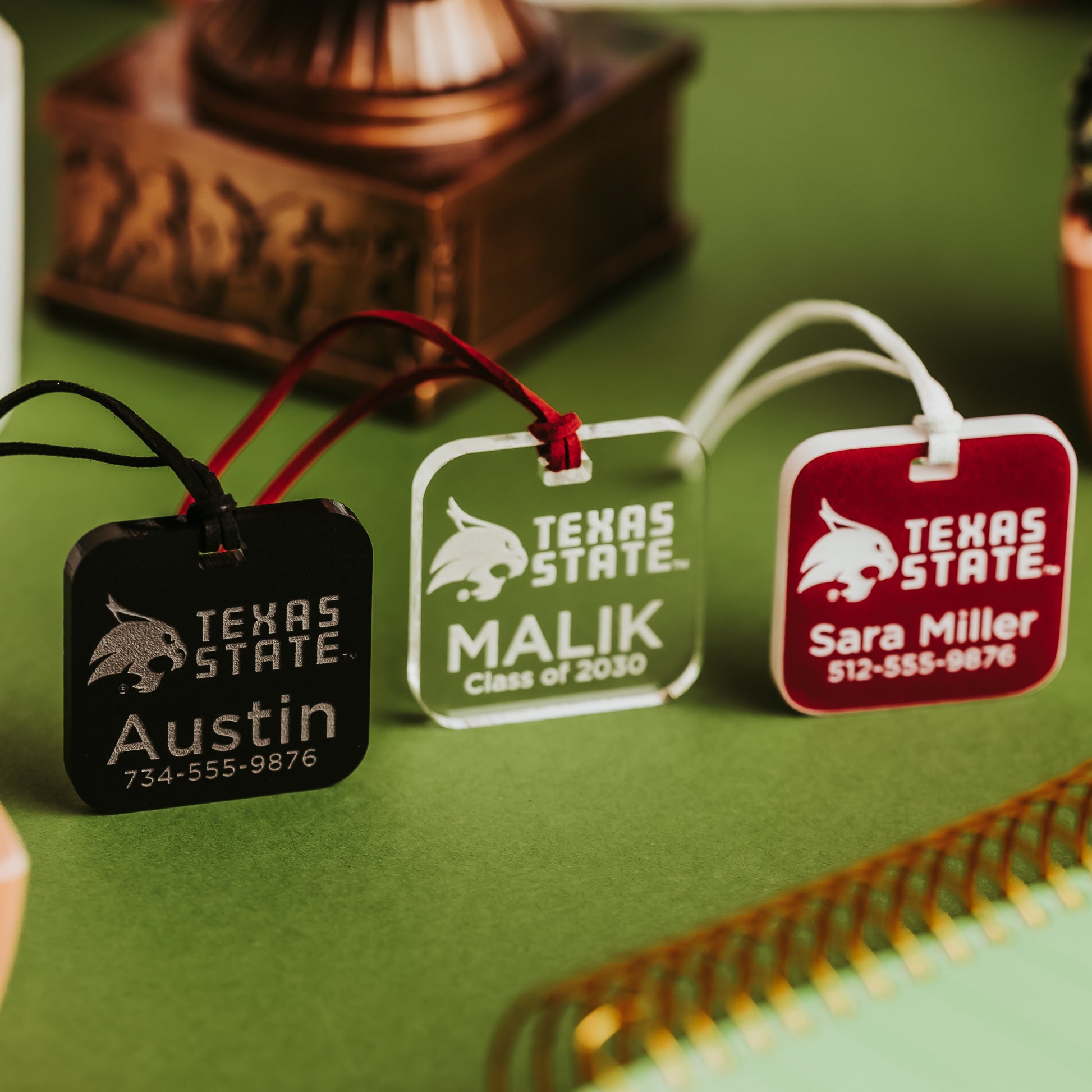 Texas State luggage tags in black, clear, and crimson acrylic, engraved with names, a class year and phone numbers
