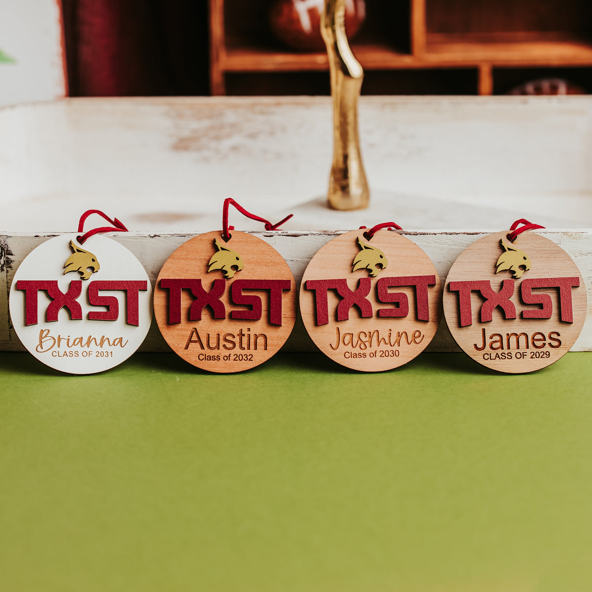 Four personalized Texas State ornaments in white, cherry, mahogany and walnut with gold Bobcat, maroon TXST and engraved names