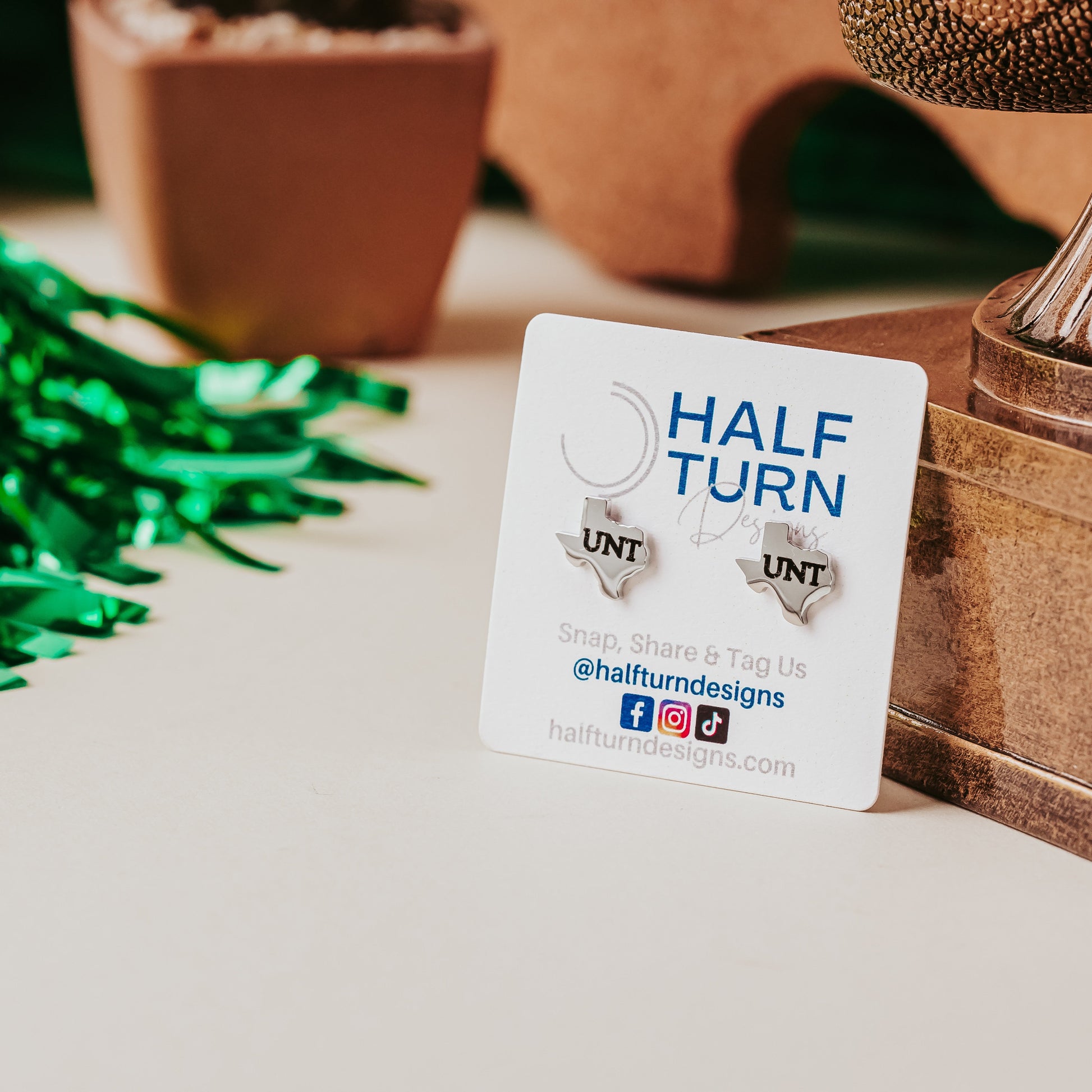 Silver Texas-shaped University of North Texas UNT stainless steel stud earrings on Half Turn Designs card