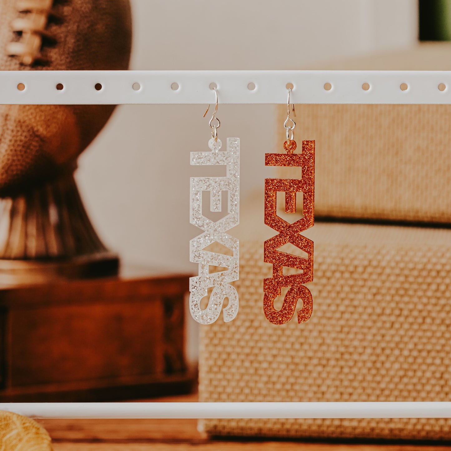 A pair of University of Texas Longhorns glitter dangle earrings on Half Turn Designs display card, featuring burnt orange and white acrylic word designs that spell “TEXAS"