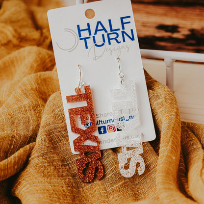 A pair of University of Texas Longhorns glitter dangle earrings on Half Turn Designs display card, featuring burnt orange and white acrylic word designs that spell “TEXAS” on silver hooks
