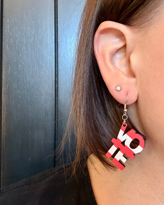 Model wearing American Flag Vote dangle earrings, wooden earrings, one in blue stars and the other in red and white stripes that each spell the word vote by Half Turn Designs.