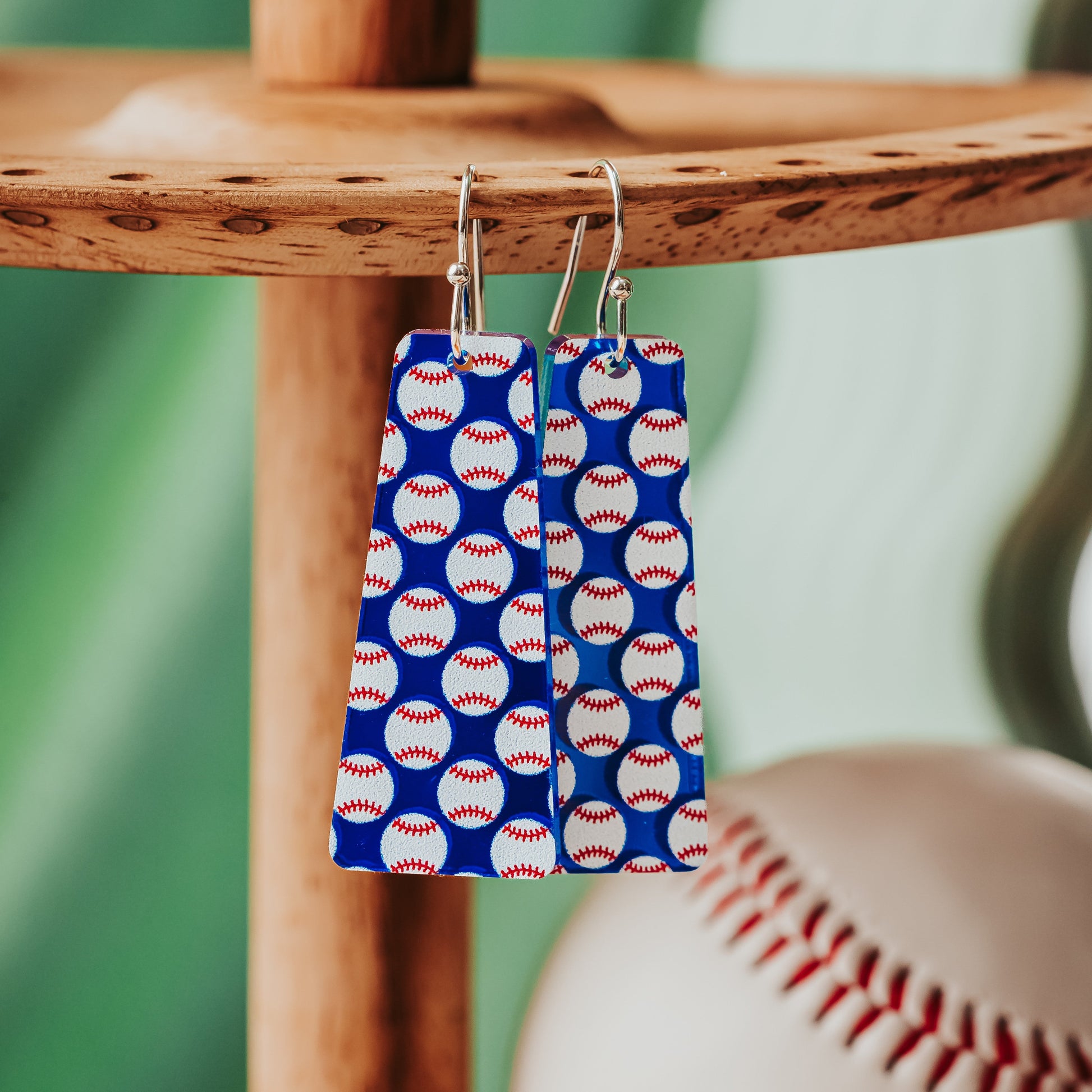 Blue mirror baseball bar dangle earrings with silver stainless steel hooks hanging on wooden stand.