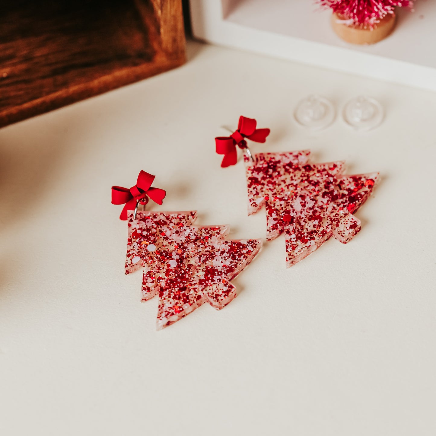 Red and white glittery Christmas tree earrings with red bow studs, lightweight with 2 inch drop length, holiday dangles styled on a neutral background.