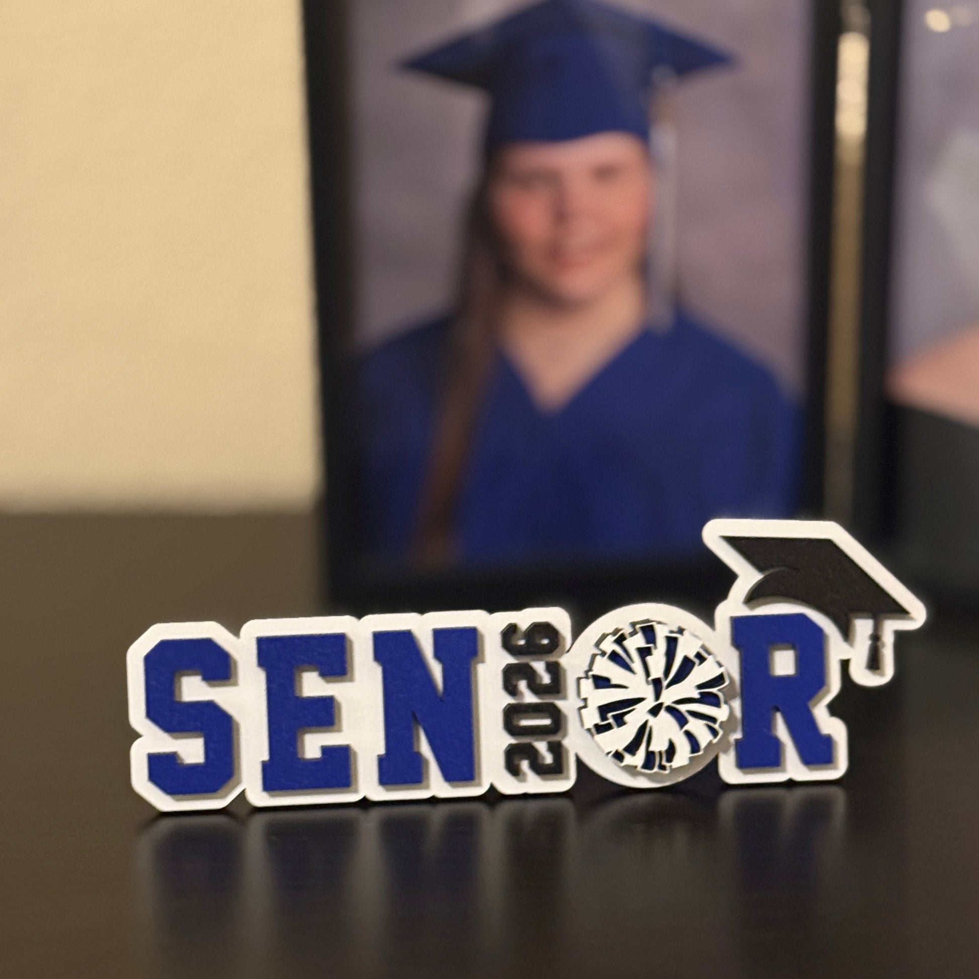 Class of 2026 gradation sign for high school girl on pom, cheerleading squad or drill team. Made from white wood with blue accents.