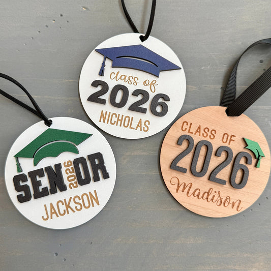 Personalized Class of 2026 ornament in white wood, engraved with the high school senior graduates name in three of the available styles from Half Turn Designs. 14 high school colors are available to further personalize the ornament with your choice of graduation cap color.