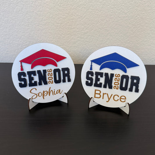 Personalized Class of 2026 senior graduation round white wooden signs with name and school accent color on white wood stand