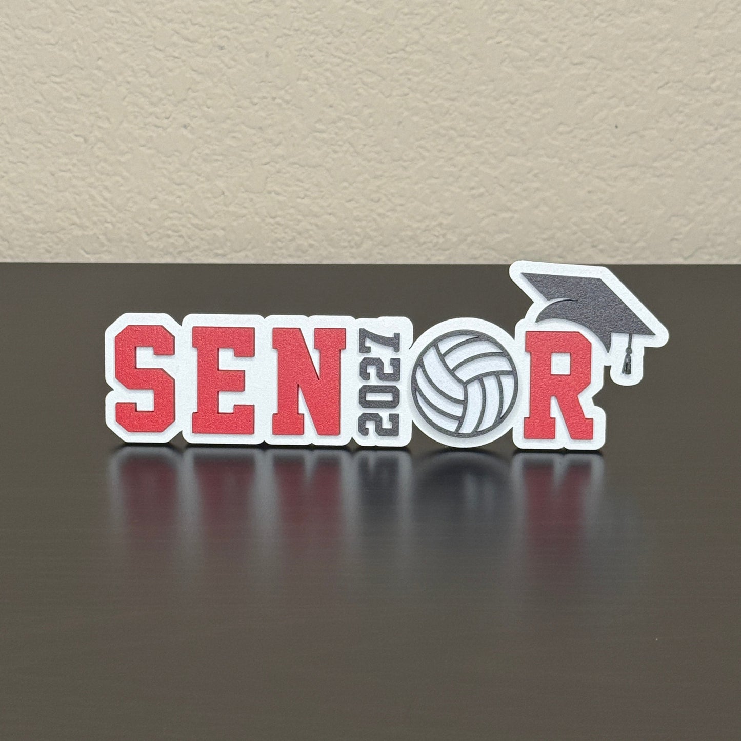 Class of 2027 volleyball senior sign with white wood base, red letters, 2027 as the I, volleyball as the O, and black cap.