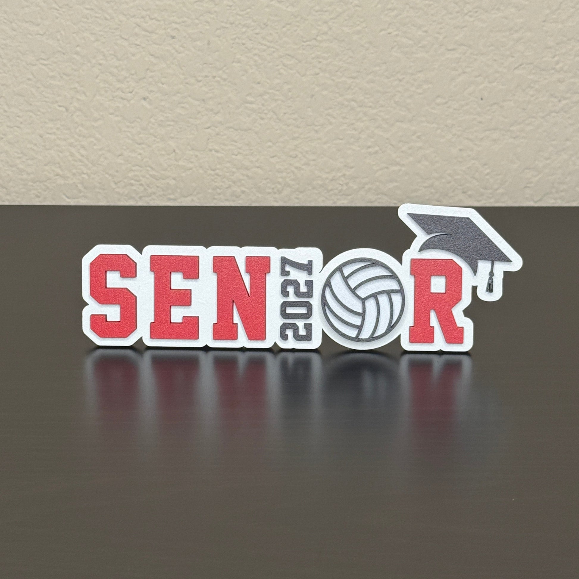 Class of 2027 volleyball senior sign with white wood base, red letters, 2027 as the I, volleyball as the O, and black cap.