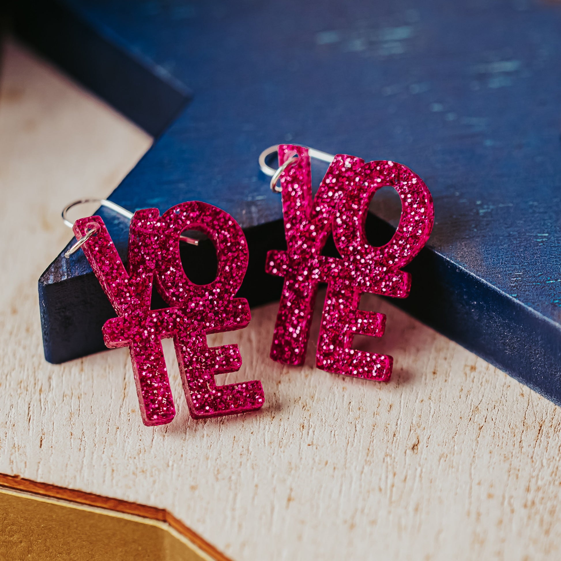 Close up of vote earrings in bright pink glitter with silver-toned earring hooks