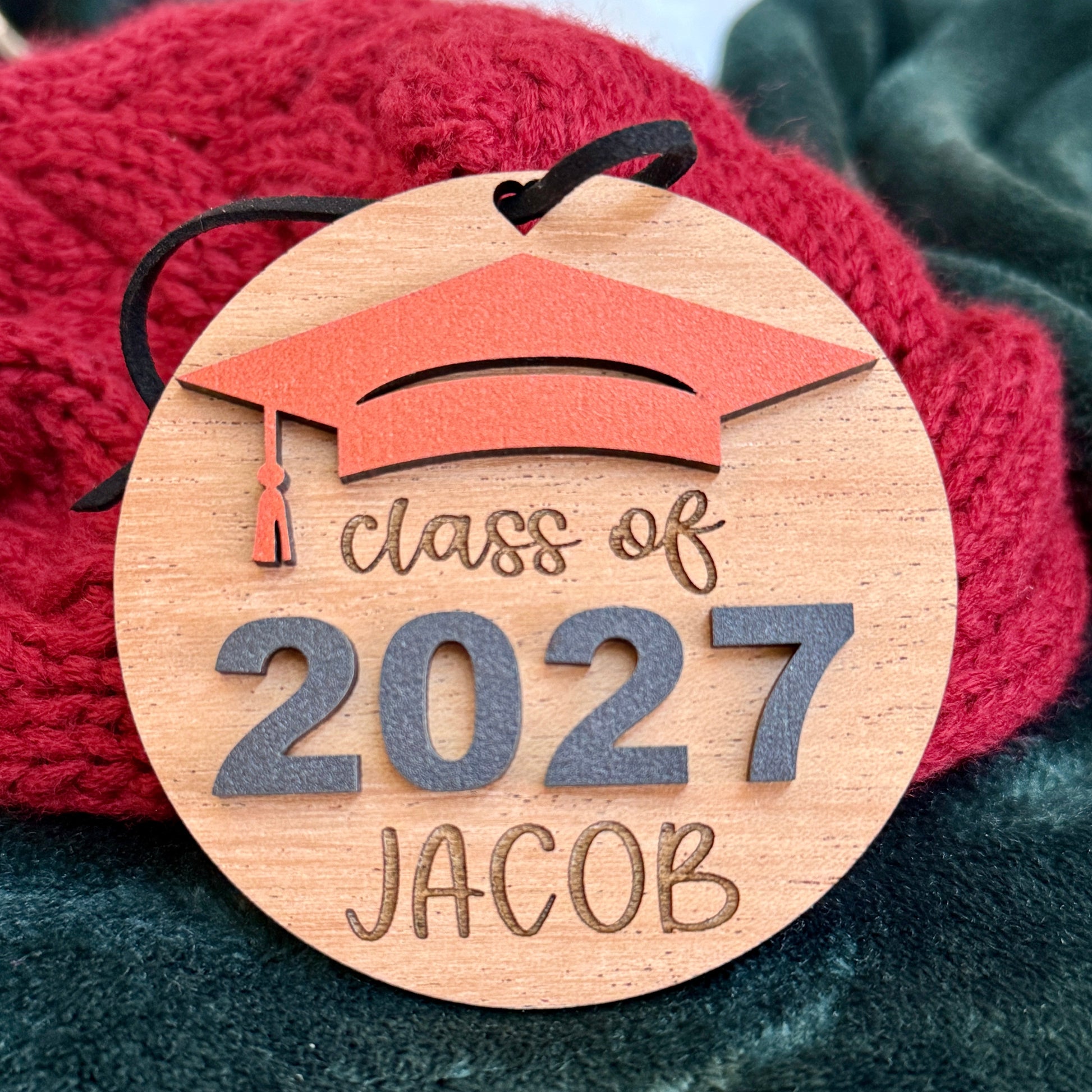 Personalized Class of 2027 wooden ornament in cherry finish with orange graduation cap, raised black 2027 numbers and graduate's engraved name