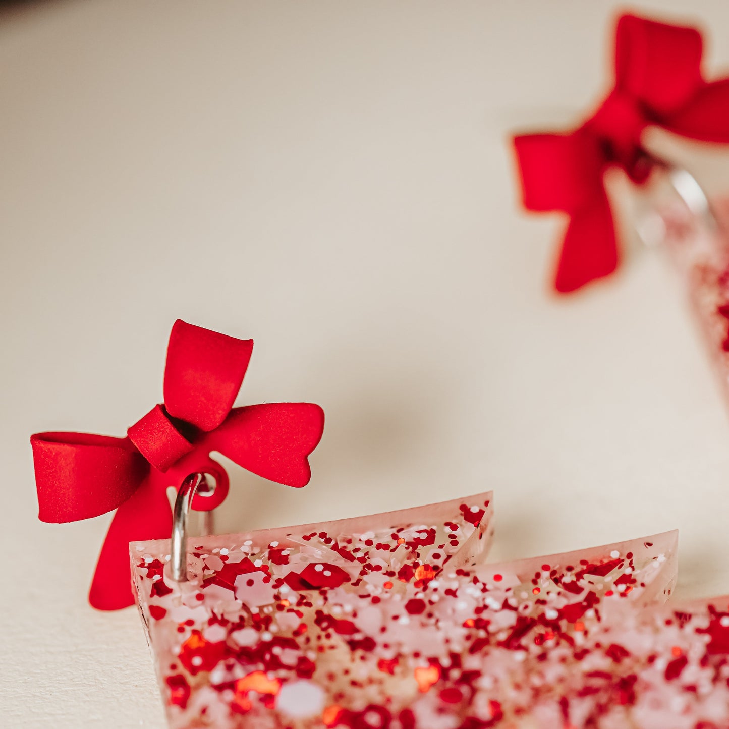 Close of red bows on Red and white glitter acrylic Christmas tree earrings with red bow studs, lightweight with 2 inch drop length, holiday dangles styled on a neutral background.