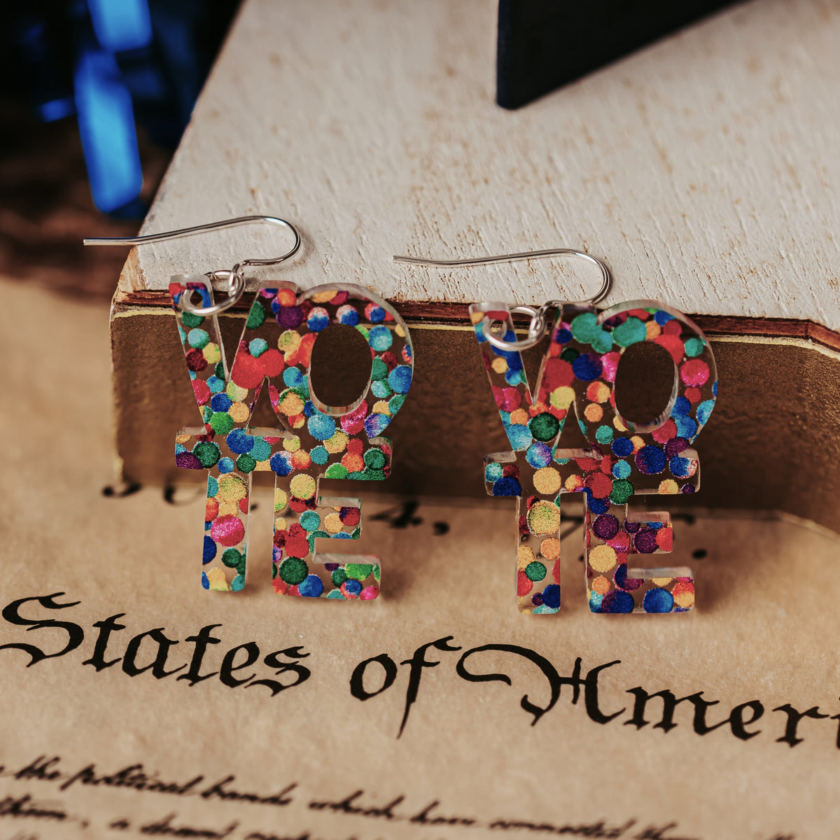 Close up of rainbow dot VOTE earrings with silver tone earring hooks