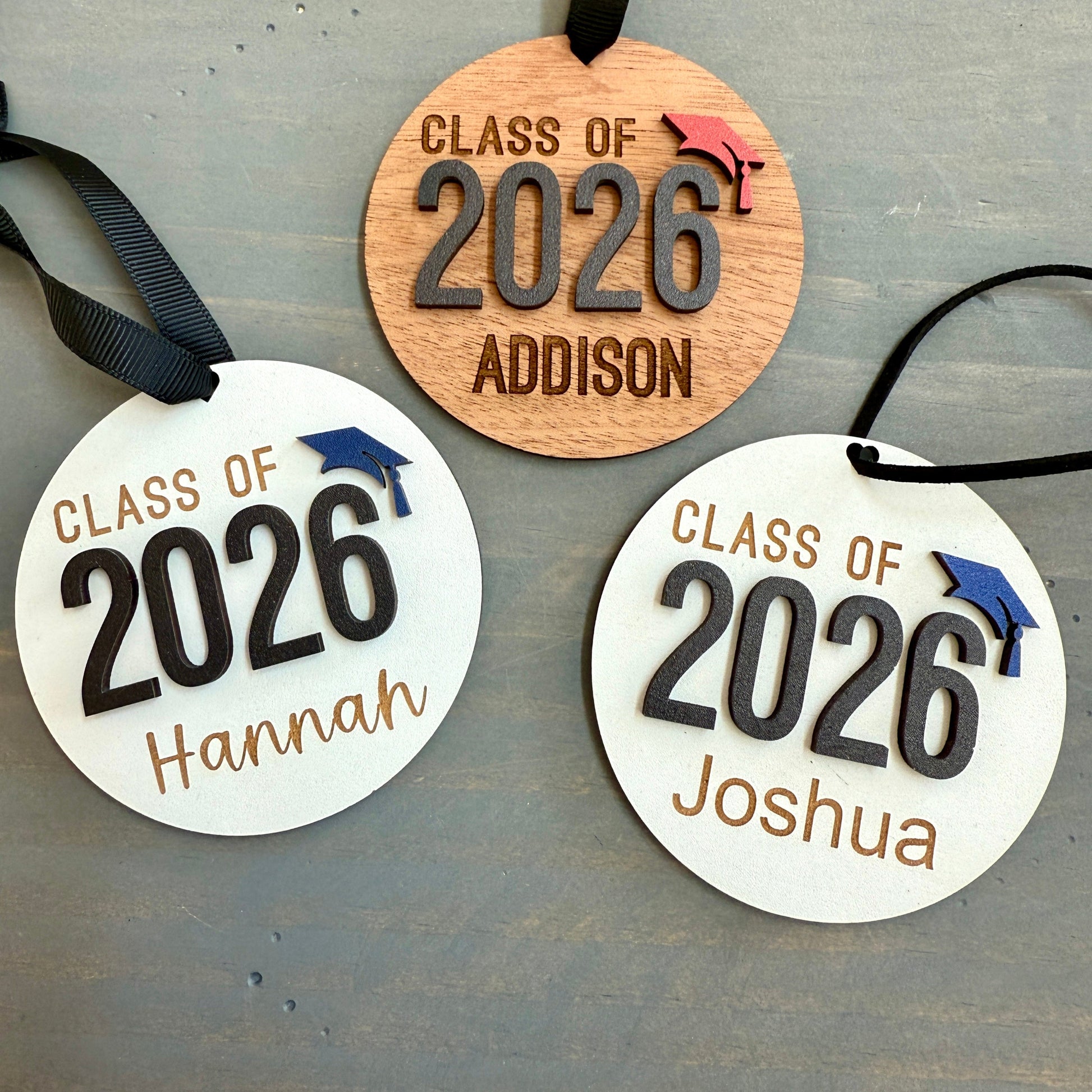 Personalized Class of 2026 ornament in white wood, engraved with the high school senior graduates name in three of the available styles from Half Turn Designs. 14 high school colors are available to further personalize the ornament with your choice of graduation cap color.