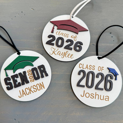 Personalized Class of 2026 ornament in white wood, engraved with the high school senior graduates name in three of the available styles from Half Turn Designs. 14 high school colors are available to further personalize the ornament with your choice of graduation cap color.