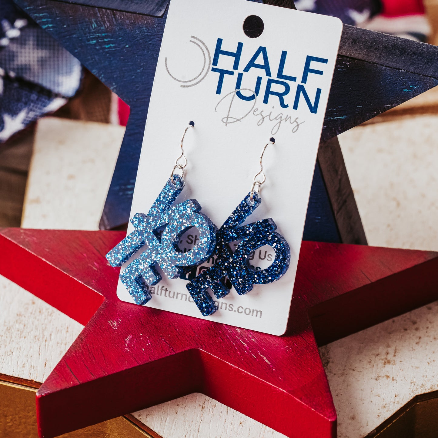 Blue glitter vote earrings with stacked VOTE letters and silver ear wires displayed on a red wooden star