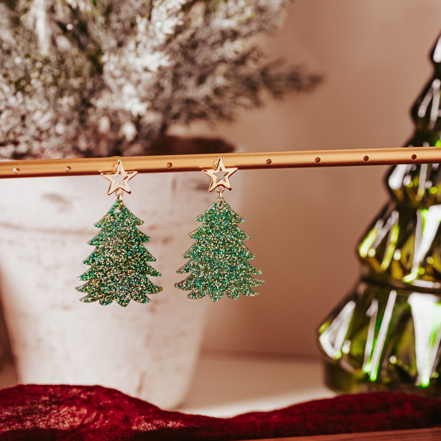 Green and gold glitter acrylic Christmas tree earrings with gold star studs hanging on display rod, showing sparkling festive dangle design by Half Turn Designs