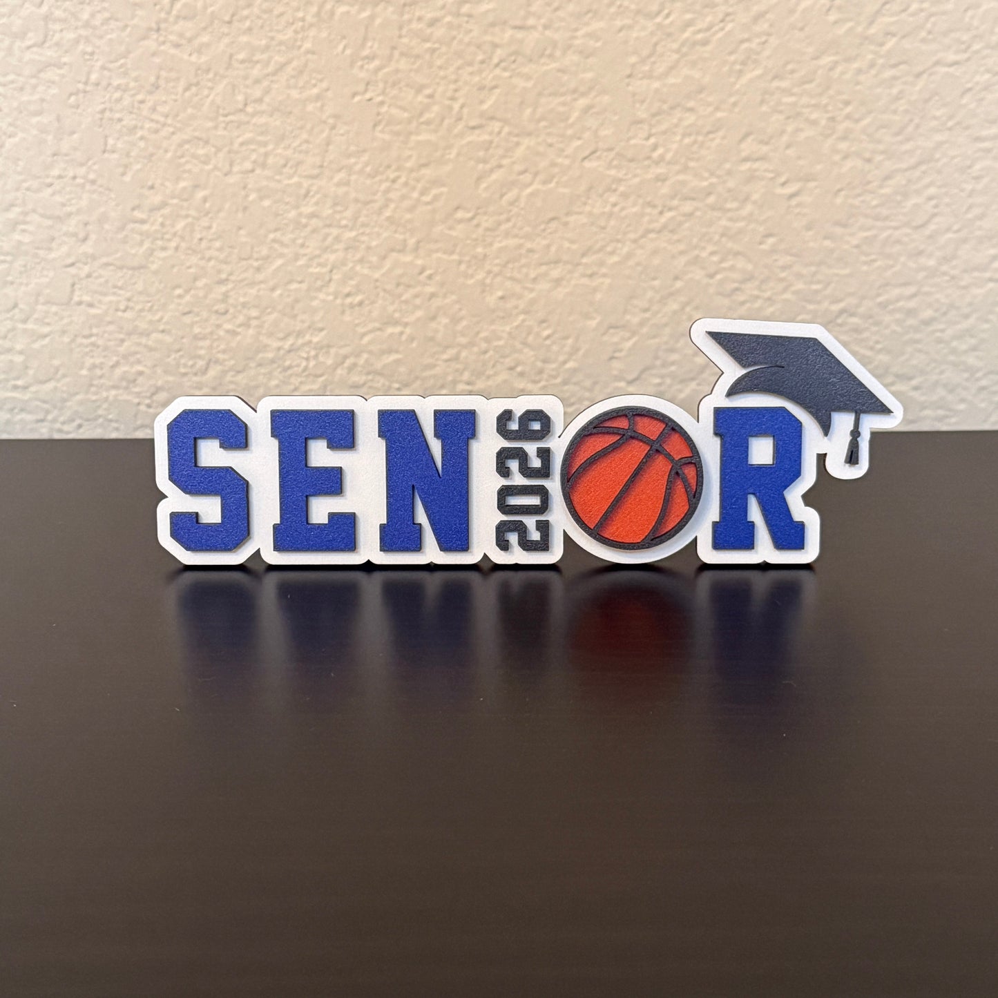 Class of 2026 senior basketball sign in blue with basketball graphic and graduation cap, custom school colors, graduation party and high school basketball banquet decor. Shown here with blue accents.