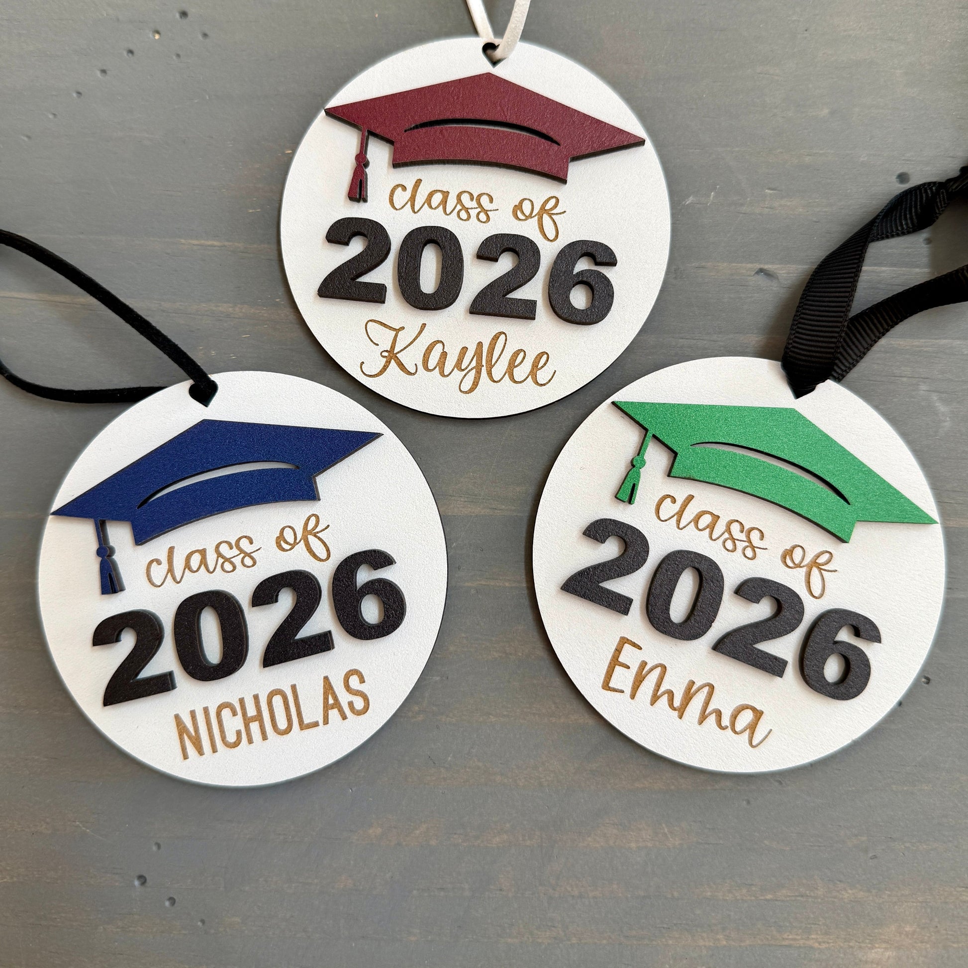 Personalized Class of 2026 ornament in white wood, engraved with the high school senior graduates name in three of the available styles from Half Turn Designs. 14 high school colors are available to further personalize the ornament with your choice of graduation cap color.