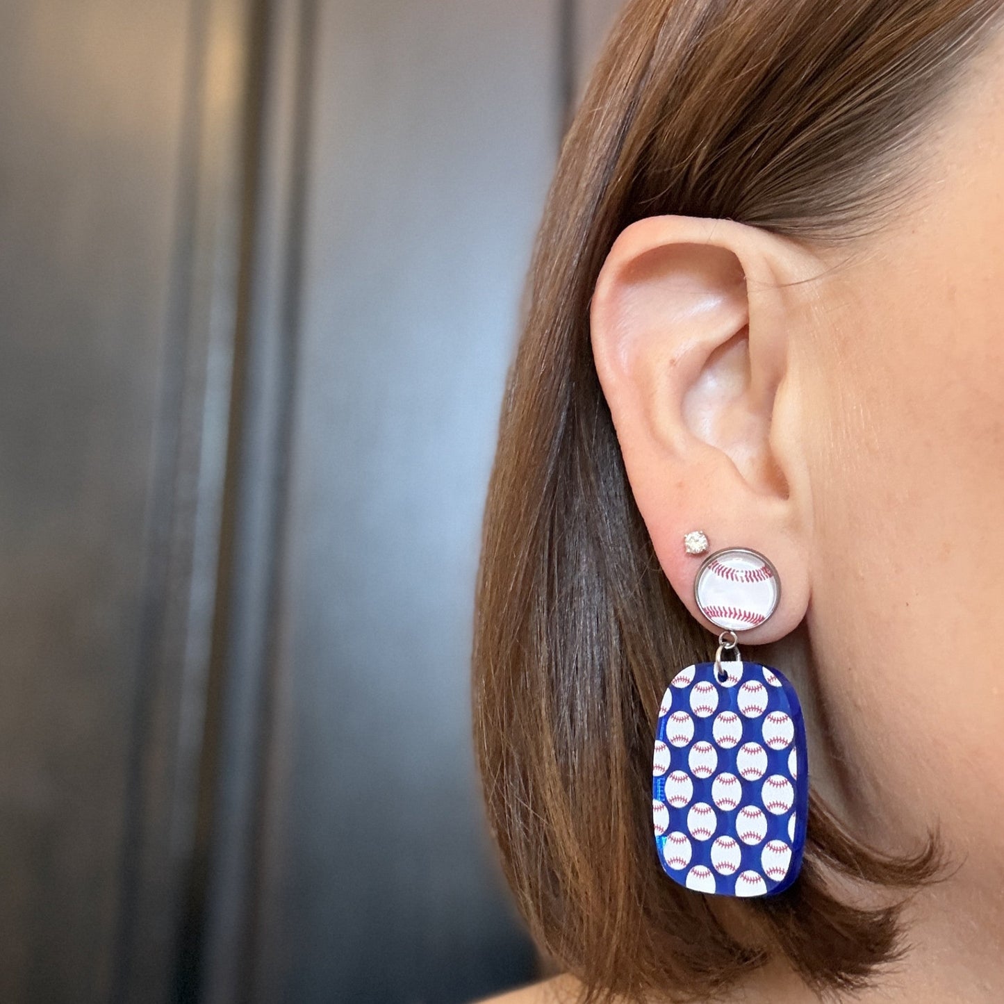 Model wearing Baseball mom earrings with blue mirror acrylic drops and repeating baseball pattern